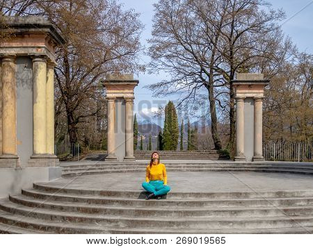 Smiling Enjoying Girl Cross-legged Sitting On The Staircase Of The Round Area With Columns, Looking 