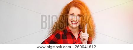 Young Red-haired Girl In A Red Checkered Shirt. Young Girl Showing Index Finger