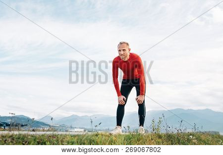 The Wide Angle Shoot Of A Man Dressed In Red Long Sleeve Shirt Very Tired After The Jog  By The Road