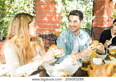Attractive Young Man Looking At Female Friend While Having Cheeseburger At Junk Food Corner
