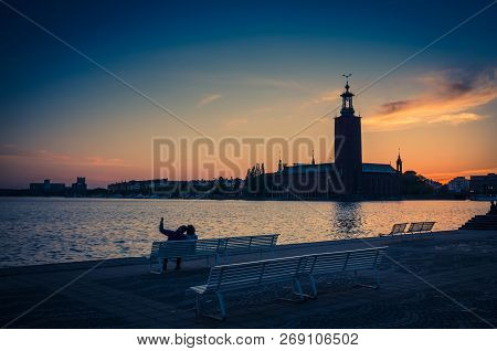 Silhouette Of Man And Woman Sitting On Bench At Promenade Quay Bank Of Lake Malaren Looking At Stock
