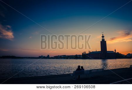 Silhouette Of Man And Woman Sitting On Bench At Promenade Quay Bank Of Lake Malaren Looking At Stock
