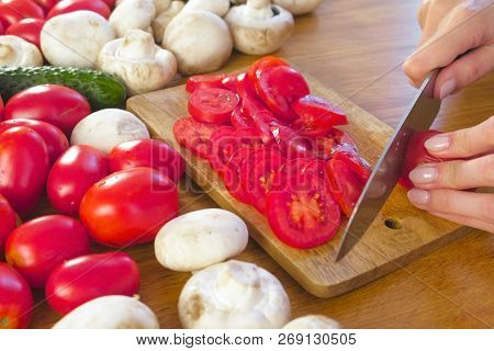 Womans Hands Is Cutting Tomatoes On The Wooden Bord On Kitchen Table. Side View.