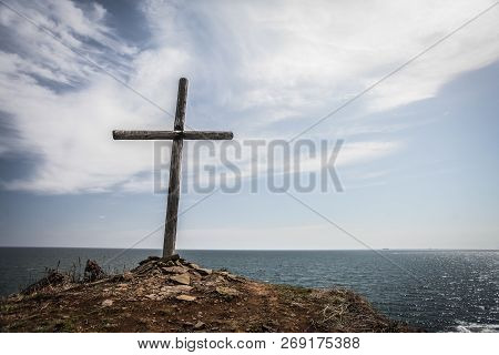 Gloomy Photo Of Old Wooden Cross On The Cliff Break, Sky And Sea Background.