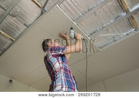 Young Man In Usual Clothing And Work Gloves Fixing Drywall Suspended Ceiling To Metal Frame Using El