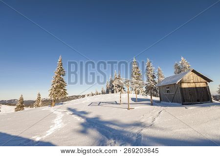 Fairy Tale Beautiful Winter Sunny Landscape. Wooden Shepherd Hut On Mountain Snowy Clearing Among Ta