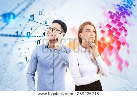 Pensive Blonde Businesswoman And Her Smiling Asian Colleague Standing Near White Wall With Digital I