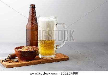 Lager Beer Pouring In Glass And Bottle With Salted Peanuts On Gray Concrete Background