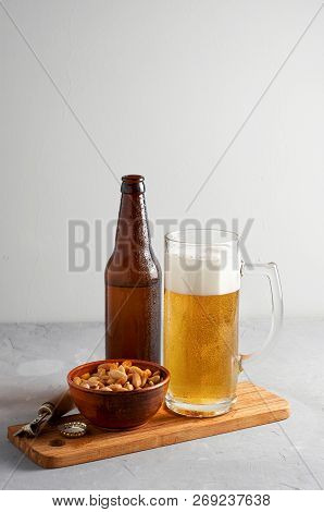 Lager Beer Pouring In Glass And Bottle With Salted Peanuts On Gray Concrete Background