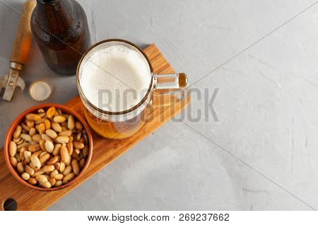 Lager Beer Pouring In Glass And Bottle With Salted Peanuts On Gray Concrete Background
