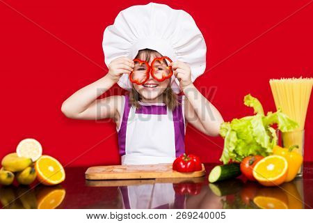 Happy Little Girl In Chef Uniform Cuts Vegetables In Kitchen. Kid Chef. Vegetarian. Cooking Process 