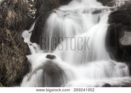 Alpine Waterfall Long Exposure Shot, Surounded By Rocks And Weeds, In Winter Time, Illustrating How 