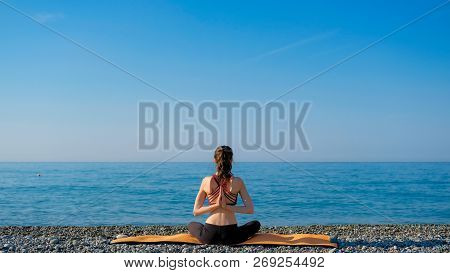 Young Slim Woman In Tight Sportswear Sitting On Orange Yoga Mat And Practicing Outdoors At Pebble Be