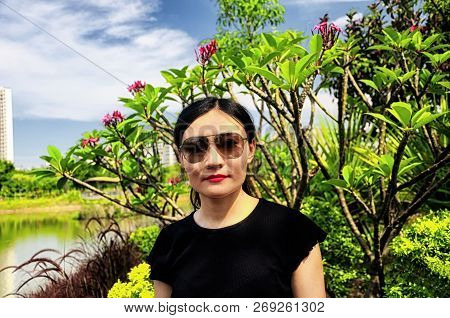 A Chinese Woman Standing In Front Of A Plumeria Rubra Or Red Frangipani Plant Within Futian Mangrove