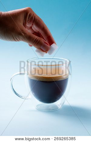 Hand Holding Two Cubes Of Sugar Over Cup Of Coffee
