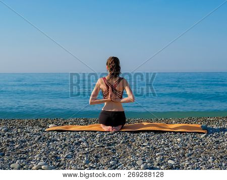 Young Slim Woman In Tight Sportswear Sitting On Orange Yoga Mat And Practicing Outdoors At Pebble Be