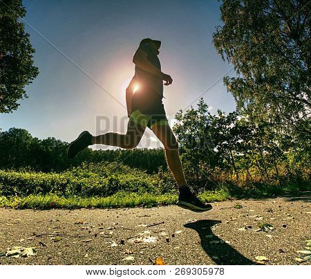 Slim Body Guy Runs On Path With Fallen Leaves. Warm Day For Outdoor Excersising.