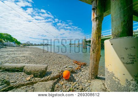 Waimea Estuary With Old Chain And Orange Buoy Lying Under Wharf Above Low Tide At Mapua South Island