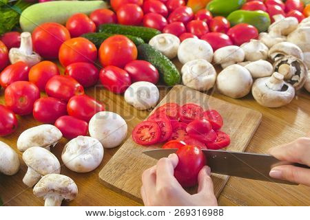 Womans Hands Is Cutting Tomatoes On The Wooden Bord On Kitchen Table. Side View.