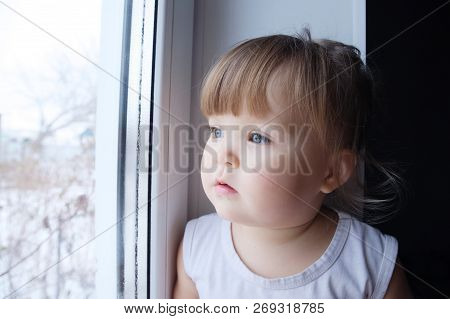 Little Child Looking Out Window. Baby Girl Longing To Walk Outdoors At Rainy Weather.