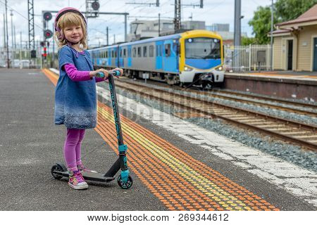 Young Girl In Pink Outfit And Pink Helmet Riding A Kick-scooter Across The Railway Line