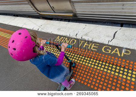 Young Girl In Pink Outfit And Pink Helmet Riding A Kick-scooter Across The Railway Line