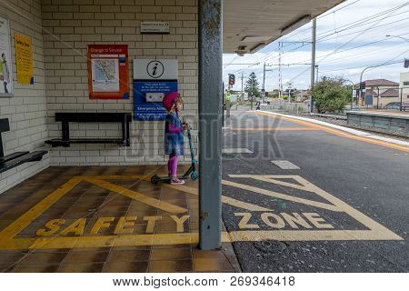 Young girl in pink outfit and pink helmet riding a kick-scooter across the railway line