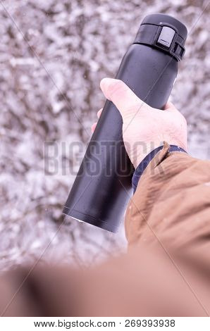 A man holds a thermos in winter. Thermos in hand. Thermos and winter. Vertical frame.
