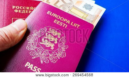 Persons Hand Holding Passports On Blue Background. Citizenship Of Estonia And Russia. Citizenship Of