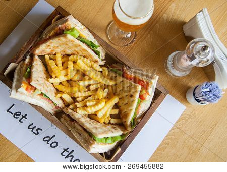 Four Small Sandwiches And French Fries In A Wooden Plate On A Table.