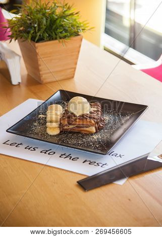 Chocolate Waffle Topped With Ice Cream And Banana Decoration On Black Plate