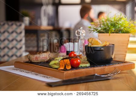Beef Steak Served With Baked Potatoes And Vegetables On A Wooden Plate In Restourant.