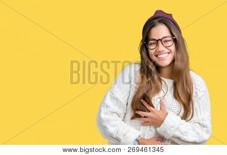 Young beautiful brunette hipster woman wearing glasses and winter hat over isolated background Smiling and laughing hard out loud because funny crazy joke. Happy expression.