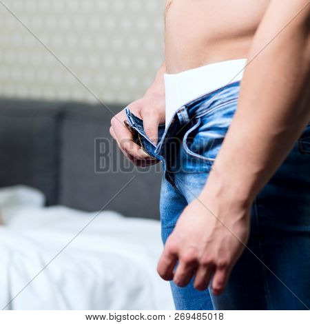 Young Man With Athletic Body Unzips His Jeans In The Bedrom.