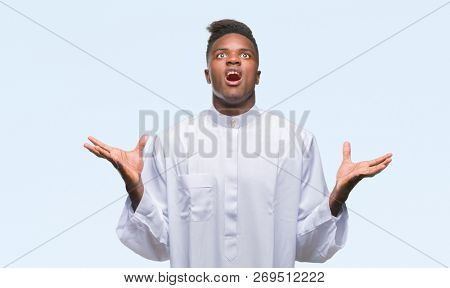 Young arabic african man wearing traditional djellaba over isolated background crazy and mad shouting and yelling with aggressive expression and arms raised. Frustration concept.