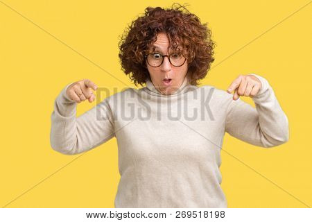 Beautiful middle ager senior woman wearing turtleneck sweater and glasses over isolated background Pointing down with fingers showing advertisement, surprised face and open mouth