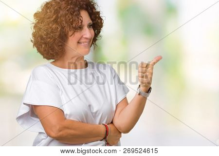 Beautiful middle ager senior woman wearing white t-shirt over isolated background Looking proud, smiling doing thumbs up gesture to the side