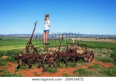Standing On A Rusting Antique Farm Tiller On The Hillside Observing The Crops Progress And With View