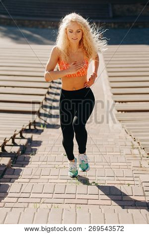 Photo Of Curly-haired Athletic Woman Running Through Park Among Benches On Summer Day. Tinting Under