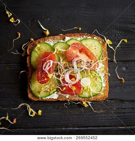 Table top view. Healthy toast with onion, cucomber, cherry tomatoes, crumbled feta cheese and radish sprouts on black wooden background