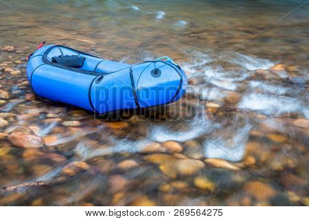 a blue pacraft (one-person light raft used for expedition or adventure racing) on a shallow, rocky t a shallow river