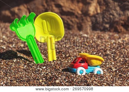 Childrens Toy Truck With Gravel Or Sand. Yellow Scoop And Green Rake On The Background. Concept Of T