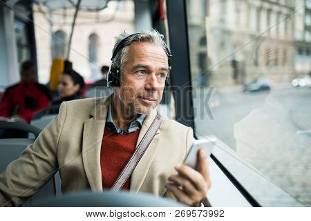 Mature Tired Businessman With Heaphones And Smartpone Travelling By Bus In City.