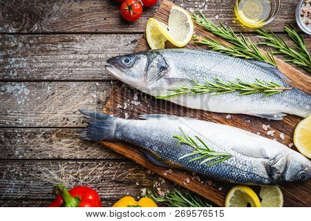 Fresh Raw Seabass And Ingredients For Cooking. Two Fish Seabass With Lemon, Spices And Herbs On Wood
