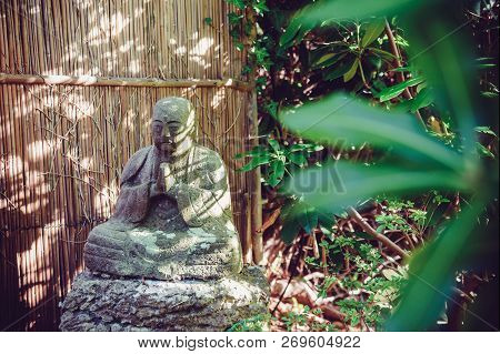 Stone Statue Of Buddhist Monk Sitting In Meditation In Japanese Garden. Exterior,outdoor Decor. Rela