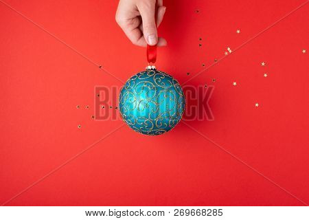Womans Hand Holding Emerald Christmas Ball With Golden Ornaments Hanging On Red Ribbon. Minimal Styl