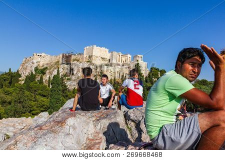 Athens, Greece - June 9, 2018: People Seated On A Rock And Chatting Against The Acropoilis Ruins In 