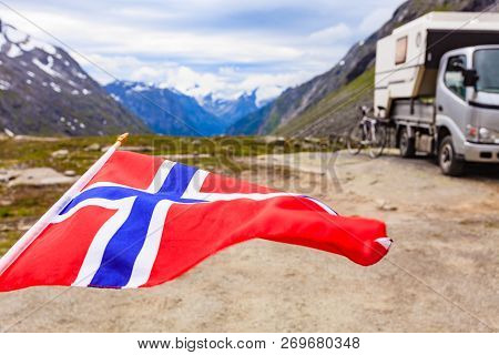 Norwegian Flag Waving On Wind And Camper Car In Mountains In The Background. Travel, Holidays And Ad