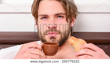 Handsome Young Man Drink Coffee And Eating Croissant In Bed. Guy Having Coffee And Holds Croissant W