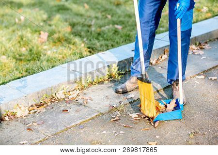 Man Sweeping Leaves With Orange Broom To The Scoop On The Street, Close-up View With No Face
